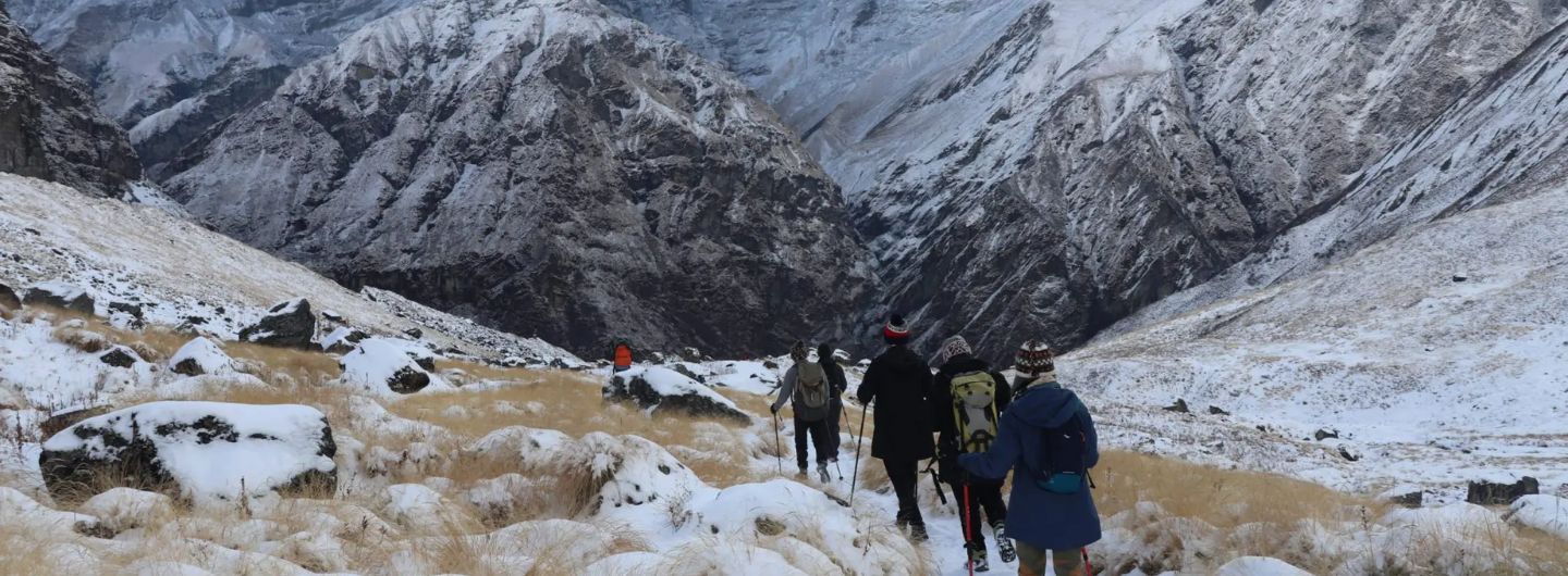 Trekkers hiking through snowy trails with rugged mountain scenery in Nepal.